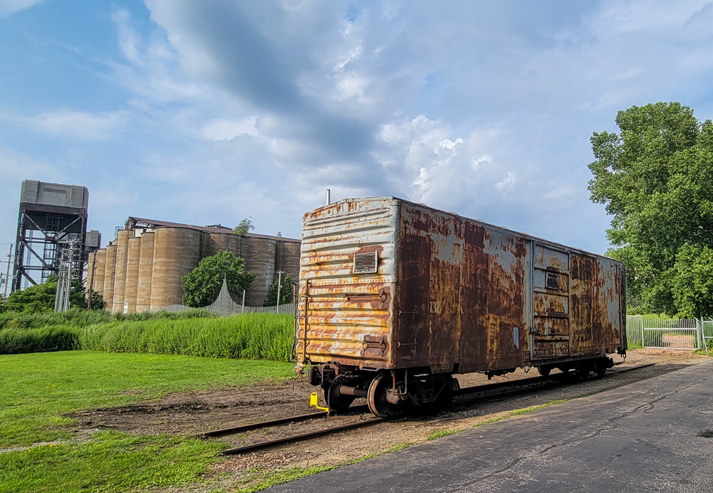 Rusted boxcar with grain silos in background