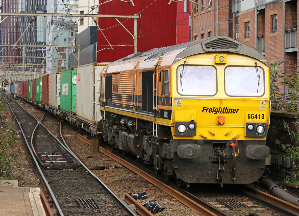 Yellow and orange locomotive pulling single-level contrainer train