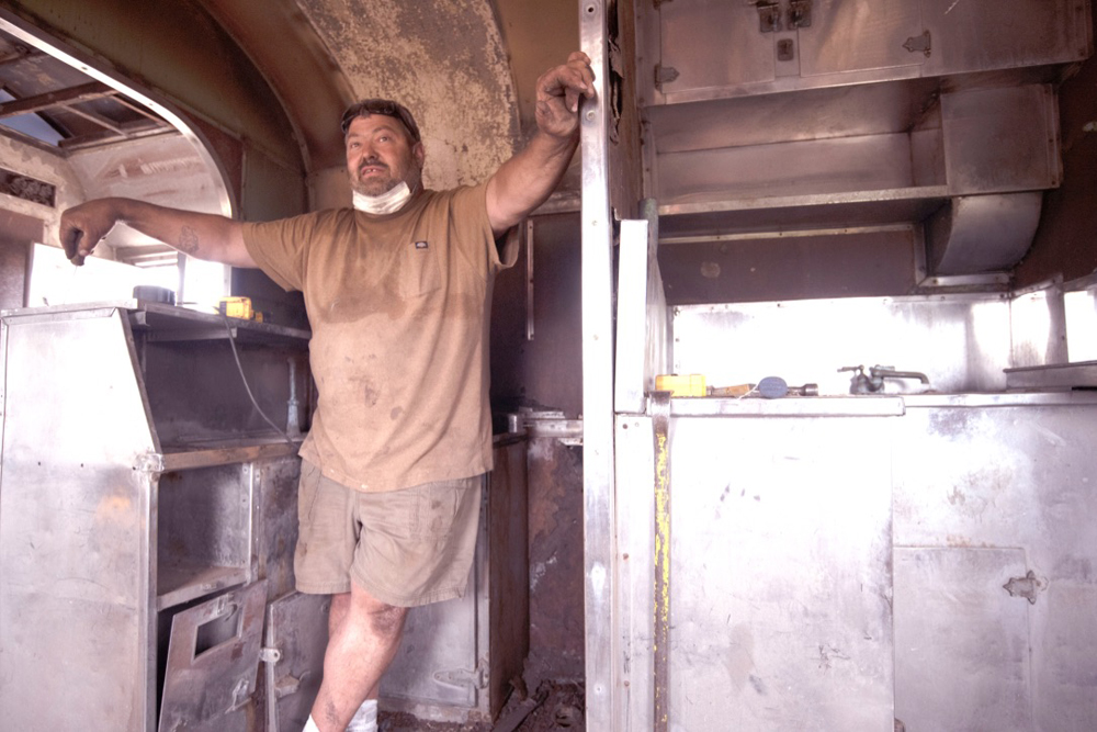 Workman in kitchen area of passenger car under restoration