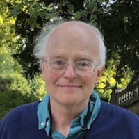 Head and shoulders of man with white hair and glasses