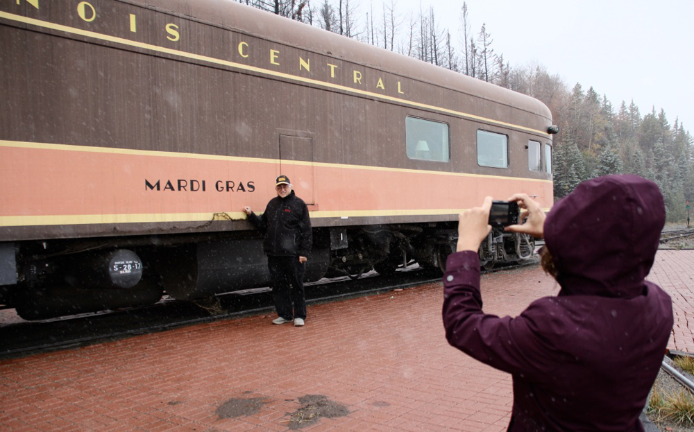 Man standing in front of brown and orange passenger car as woman takes photo