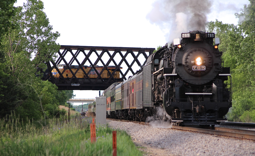 Passenger train with steam engine stops on straight as diesel crosses bridge in background