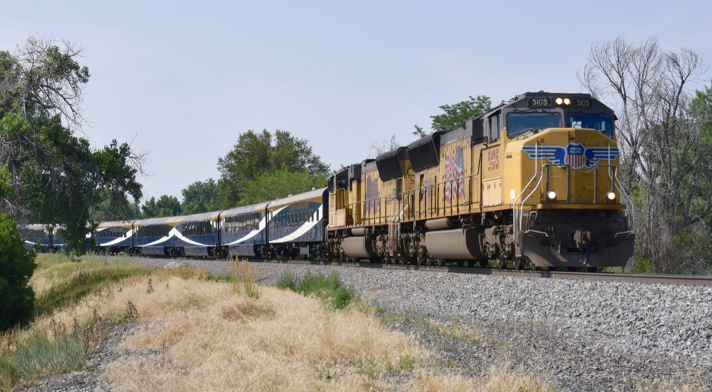 Two yellow locomotives leading blue, gold, and white passenger cars