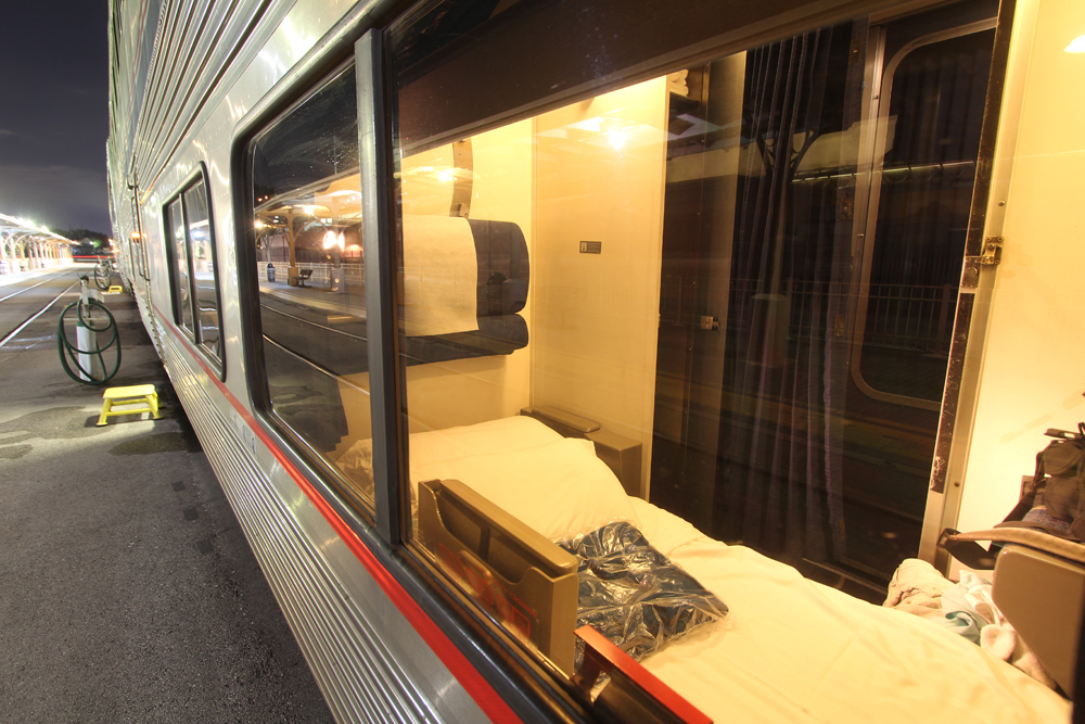 Looking through window into compartment of sleeping car with bed made for the night