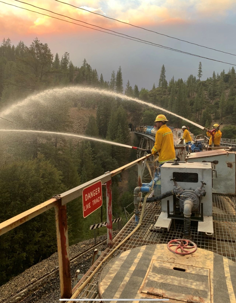 Men spraying water off train on bridge under smoky skies