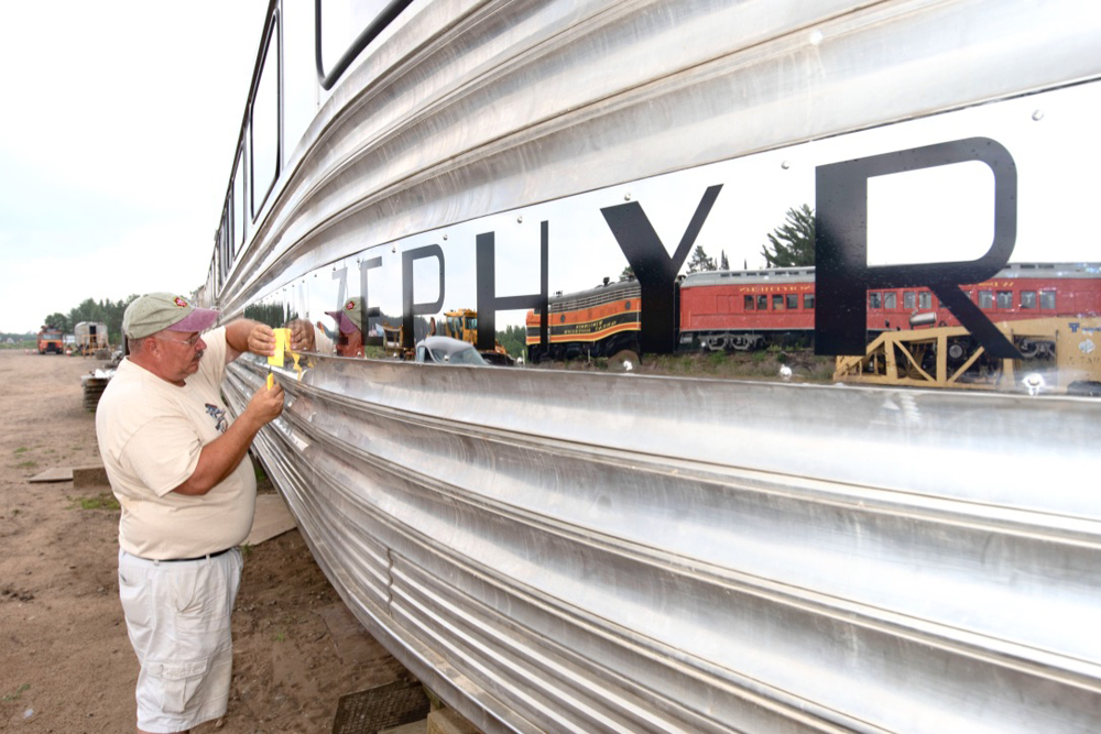 Man works on side of stainless steel passenger car