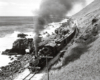 Black-and-white overhead view of steam locomotive with freight train beside ocean