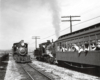 Black-and-white view of two steam locomotives meeting, with sailors looking out from coach