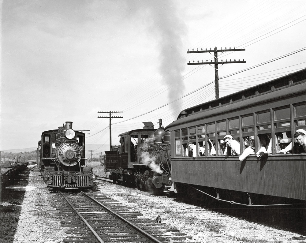 Black-and-white view of two steam locomotives meeting, with sailors looking out from coach