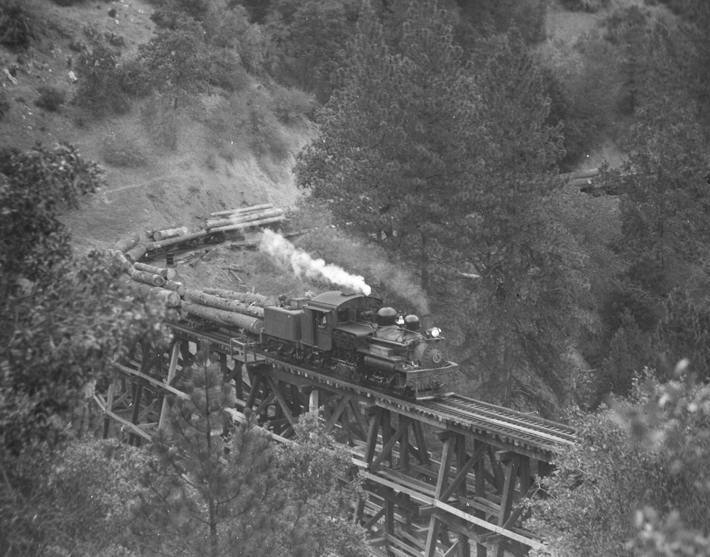 Black-and-white overhead view of Shay steam locomotive crossing trestle with log train