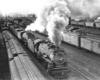 Black-and-white overhead view of steam locomotive with freight train in freight yard