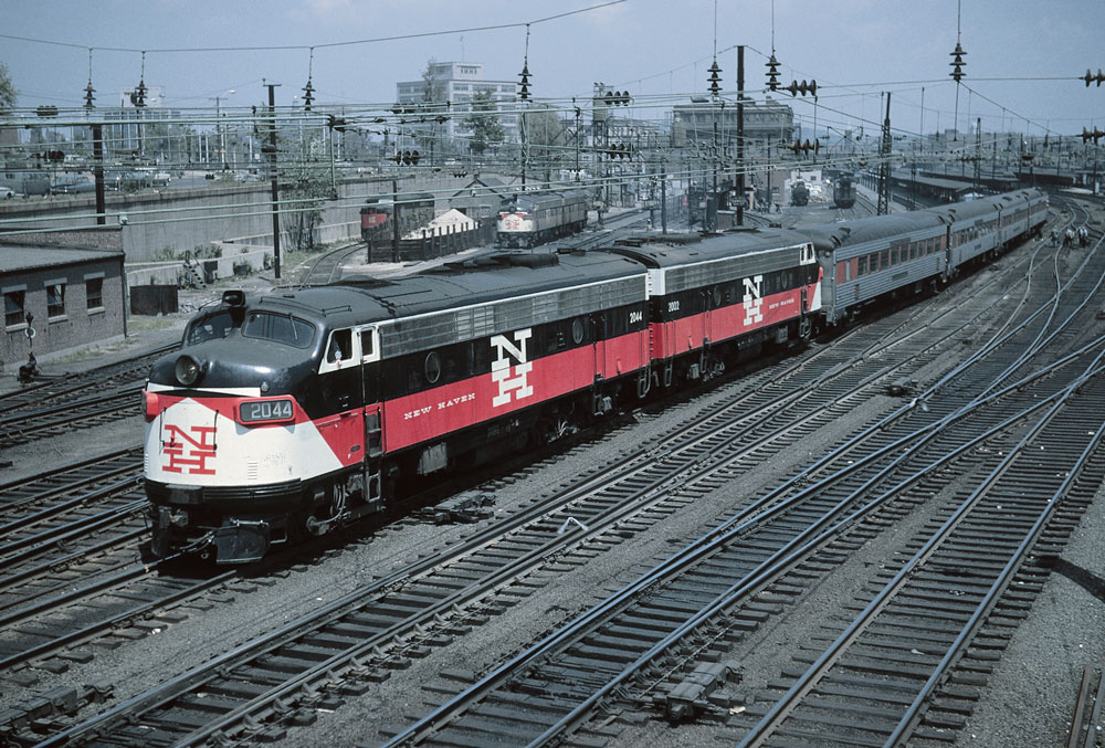 Overhead color photo of two streamlined diesel locomotives departing station with passenger train