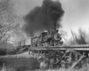 Black-and-white view of 4-6-0 steam locomotive crossing wood trestle with freight train