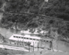 Black-and-white overhead view of streamlined diesel locomotives with freight train passing hydroelectric plant