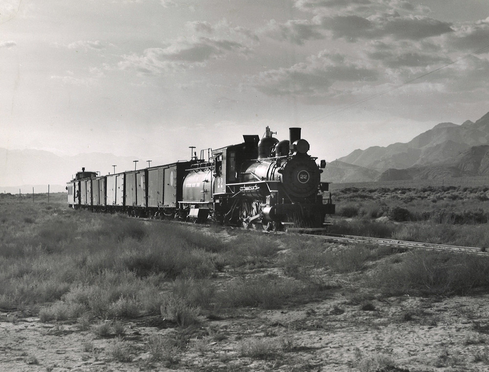 Black-and-white view of 4-6-0 steam locomotive with short freight train in desert
