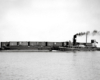 Black-and-white broadside view of tugboat with barge carrying freight cars