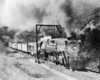 Black-and-white view of steam locomotive with freight train in mountains