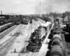 A steam locomotive hauling a freight train out of a rail yard.