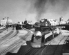 A streamlined steam locomotive leads a passenger train away from a passenger area toward the camera lens.