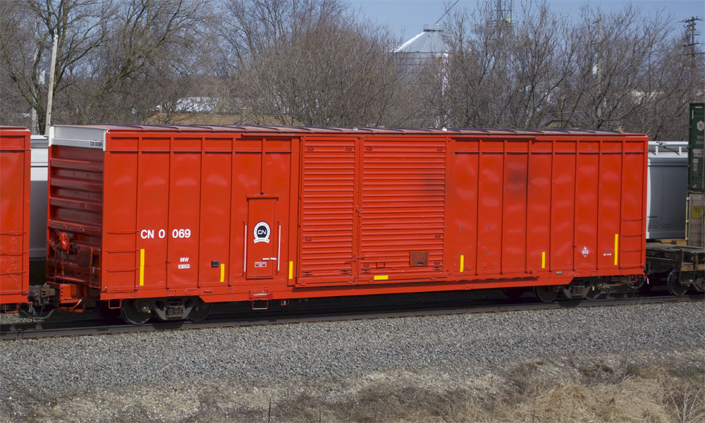 A bright red-orange Canadian National boxcar is seen in the middle of a freight train.