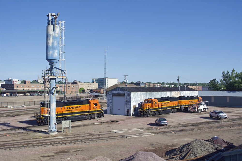 Metal enginehouse and sand tower with three BNSF Ry. road locomotives parked by building.