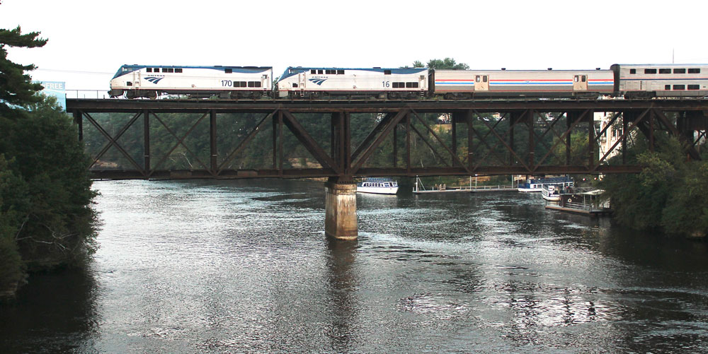 passenger train on bridge over lake with boats beneath