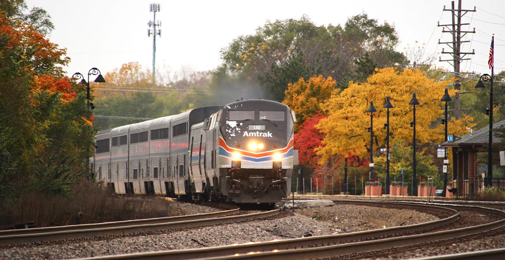 Passenger train near station among trees in fall.