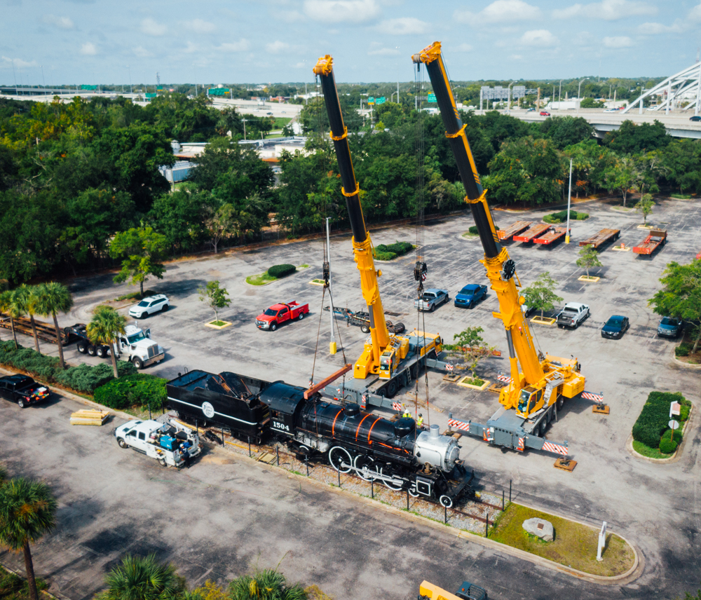 Cranes and steam locomotive in parking lot