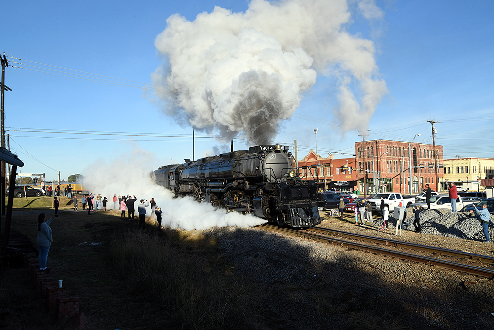 Steam locomotive sprays steam on spectators in a downtown setting