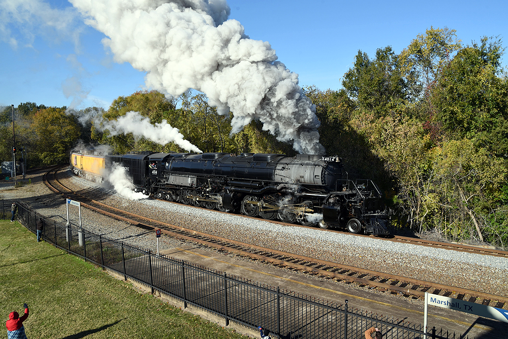 Fence separates spectators from steaming and smoking steam locomotive on curve