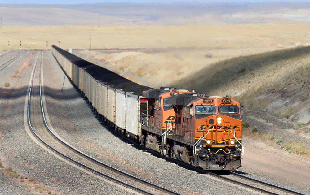 Two locomotives pulling train in large vista of open spaces