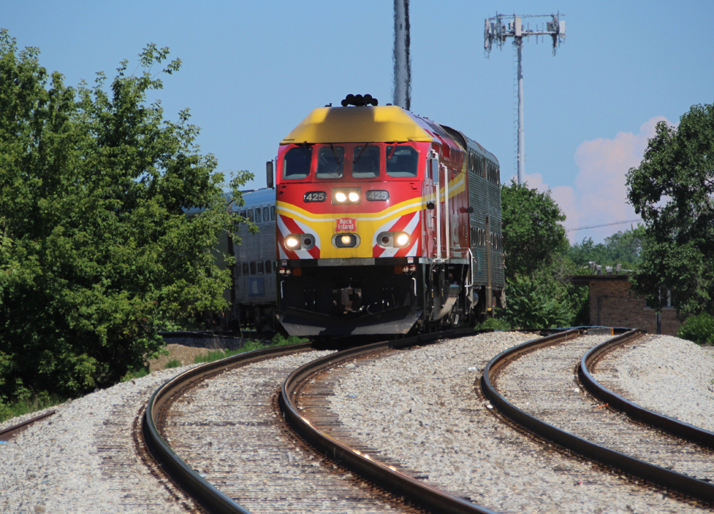 Red and yellow locomotive brings commuter train around sharp curve