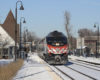 Train stops at station on cold, sunny day with snow covering the ground.