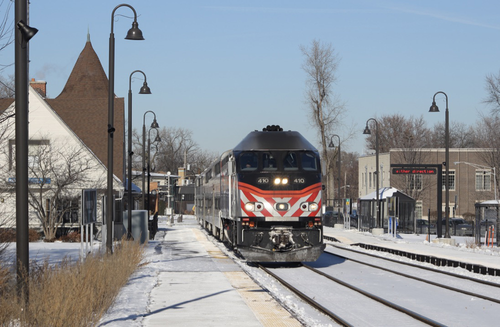Train stops at station on cold, sunny day with snow covering the ground.