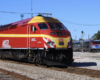 Train with red and yellow locomotive in foreground; train with blue, black, white, and silver locomotive in background.