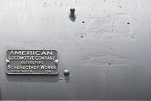 Metal plate reading “American Locomotive Company” with date and serial number; bolt holes nearby show former locations of earlier versions of plate.