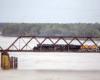 Large steam locomotive on a truss-type steel bridge over a river.