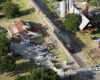 Steam locomotive passing between rural steel buildings a small crowd of people.