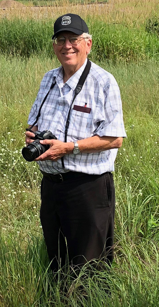 Man in black cap with camera standing in field