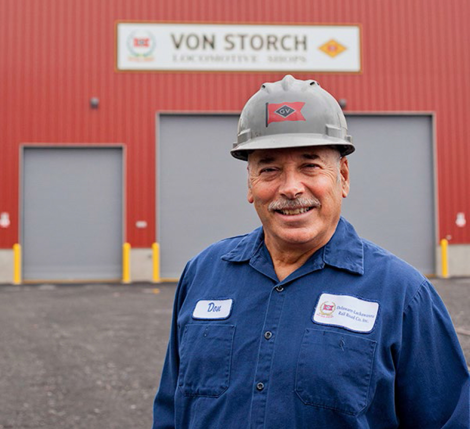 Man with hard hat in blue shirt, standing in front of shop building