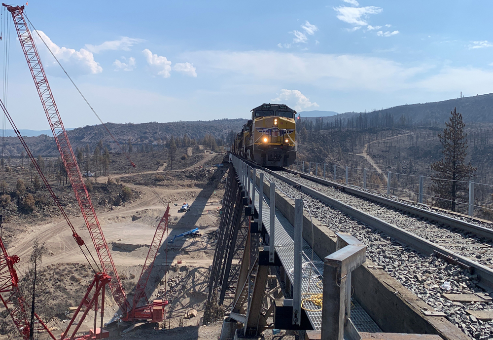 Train crossing bridge next to construction equipment