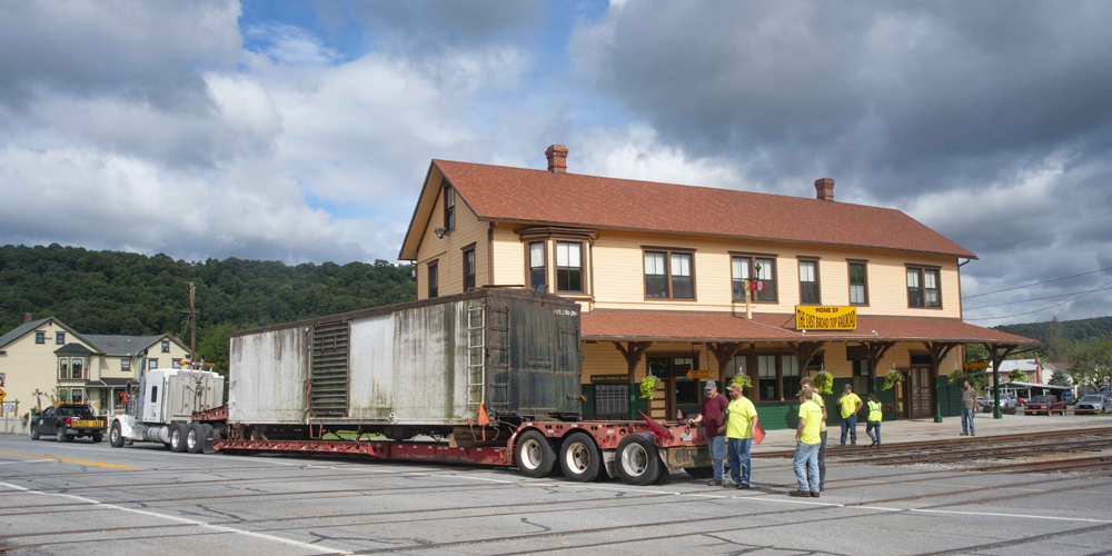 Boxcar on truck trailer next to station building