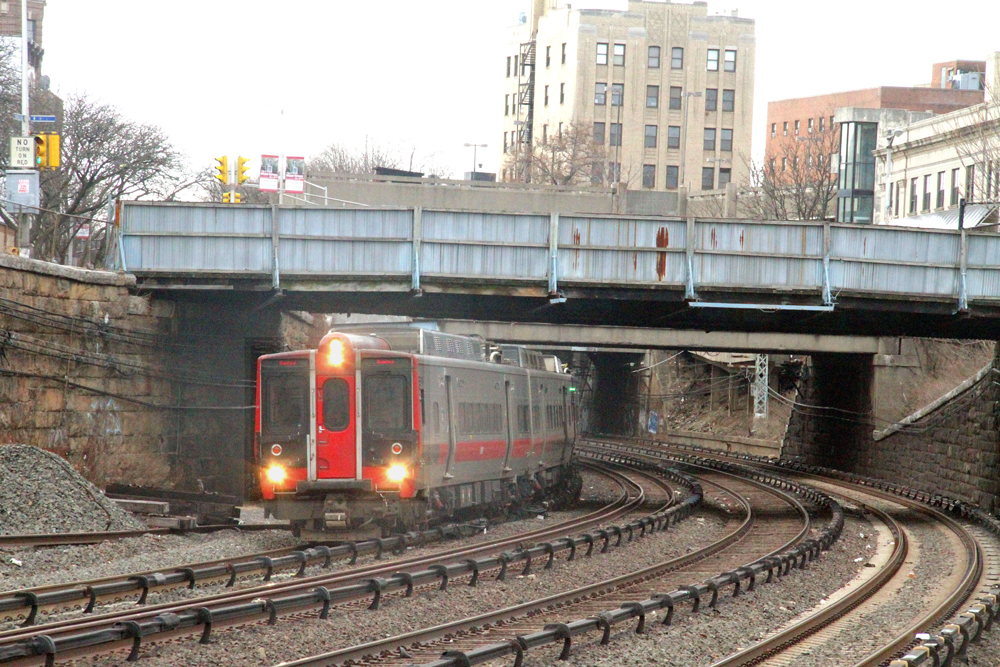 Electric commuter train passing under wood-sided bridge