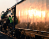 Close-up view of a steam locomotive tender reflecting low angle sunlight as a railroader climbs into a steam locomotive cab.