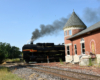 Steam locomotive nosing past old brick passenger station.