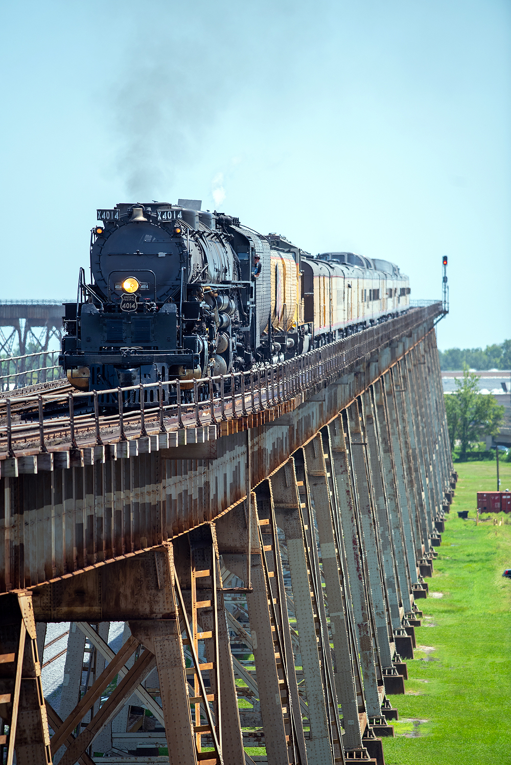 Large steam locomotive with train on long bridge seen with telephoto lens.