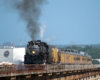 Steam locomotive and yellow passenger train on a long bridge deck.