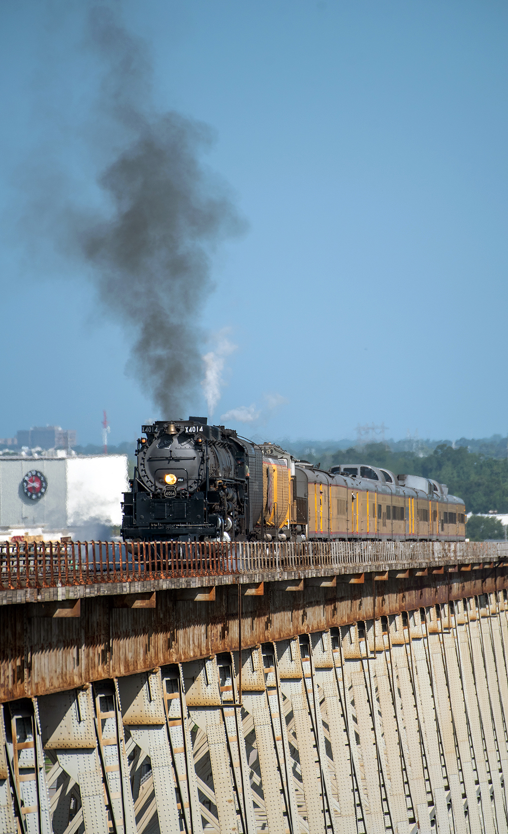 Steam locomotive and yellow passenger train on a long bridge deck.