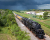 Large steam locomotive hauling train under clouded skies with a storm in the far distant background.