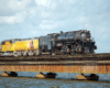 Large steam locomotive and train cross a causeway over water.